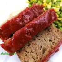 Sliced meatloaf shown with peas and corn.